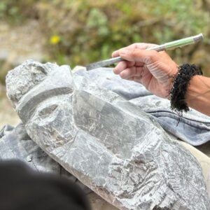 Eine Hand mit einem Werkzeug arbeitet an einer Steinskulptur