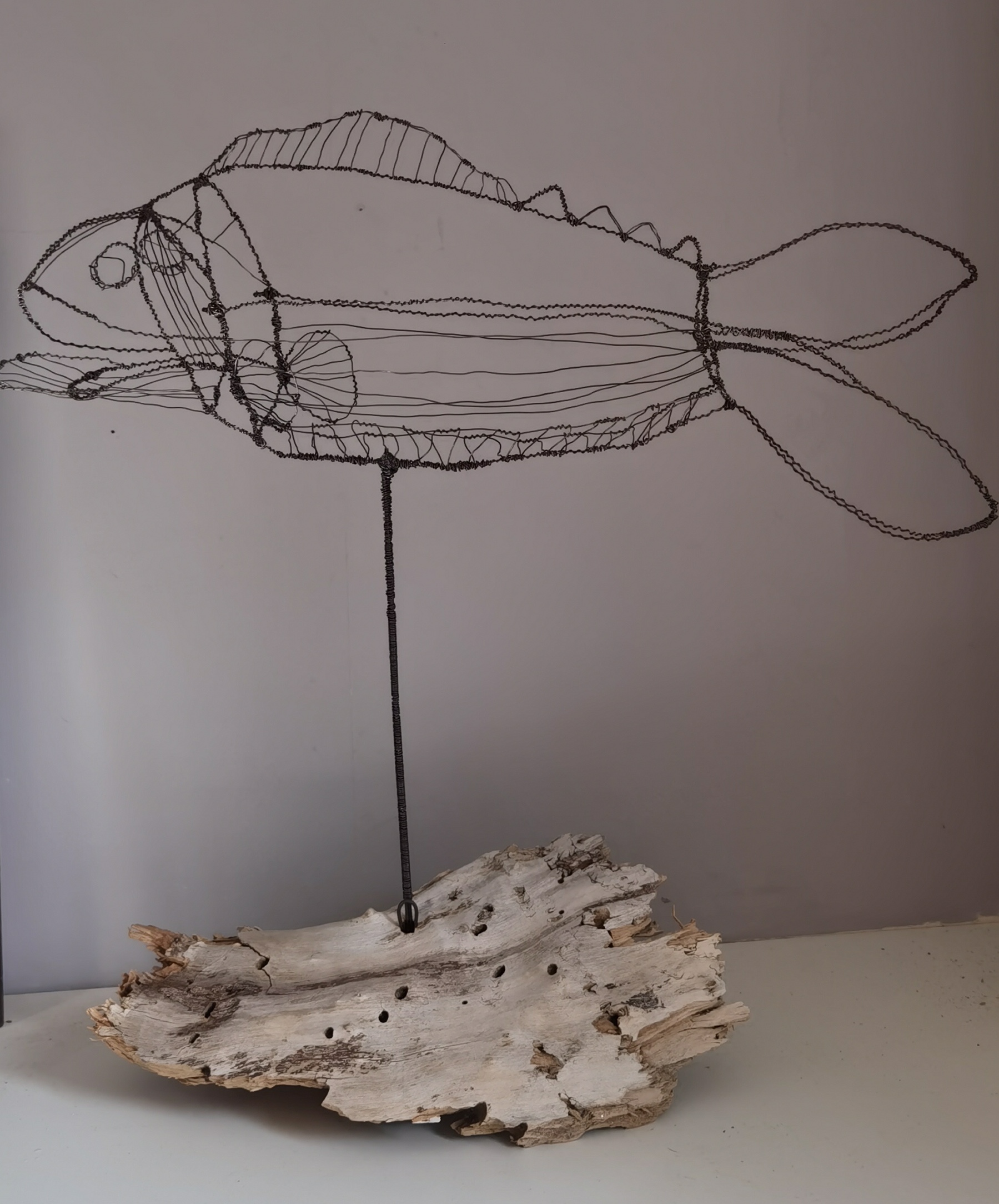 Drahtobjekt in Fischform auf Holzstück